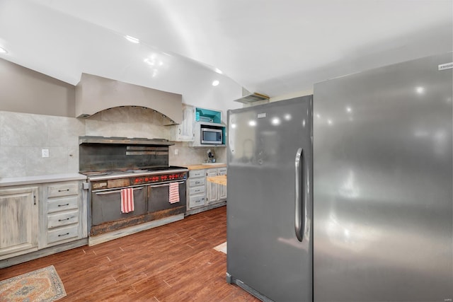 kitchen with custom exhaust hood, light wood-type flooring, light countertops, decorative backsplash, and appliances with stainless steel finishes