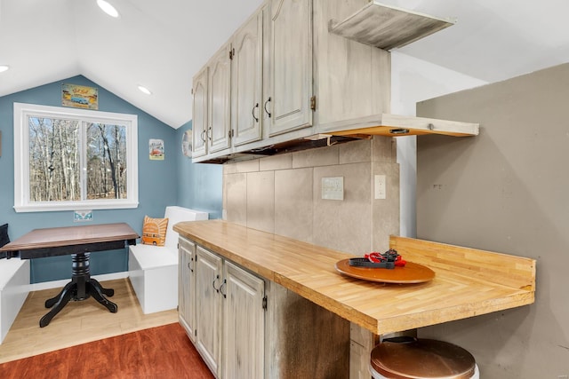 kitchen featuring tasteful backsplash, vaulted ceiling, butcher block counters, dark wood-type flooring, and a breakfast bar area