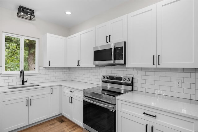 kitchen with light wood-style flooring, light countertops, backsplash, appliances with stainless steel finishes, and a sink
