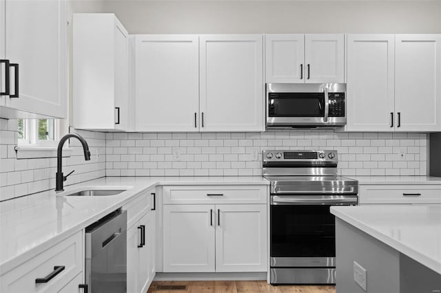 kitchen featuring decorative backsplash, white cabinetry, a sink, and appliances with stainless steel finishes
