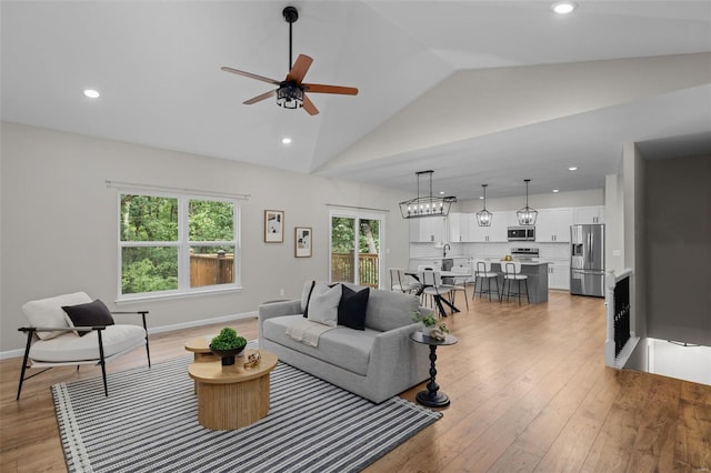 living area featuring baseboards, light wood-type flooring, vaulted ceiling, and a ceiling fan