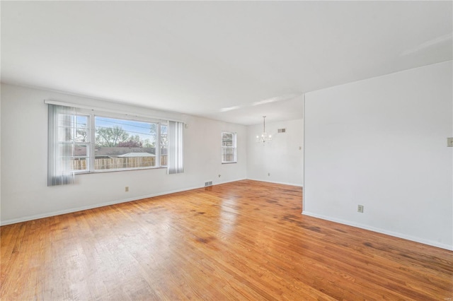 spare room with visible vents, light wood-style flooring, an inviting chandelier, and baseboards