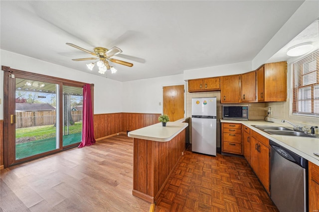 kitchen with freestanding refrigerator, stainless steel dishwasher, black microwave, a sink, and brown cabinets