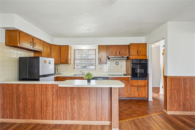 kitchen with brown cabinetry, a peninsula, light countertops, and black appliances