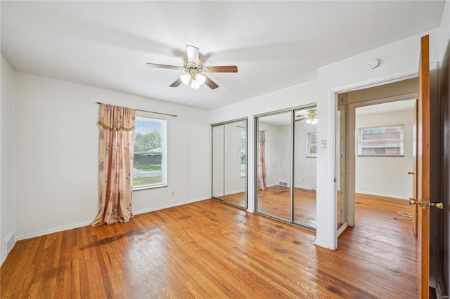 unfurnished bedroom featuring ceiling fan, two closets, light wood finished floors, and baseboards