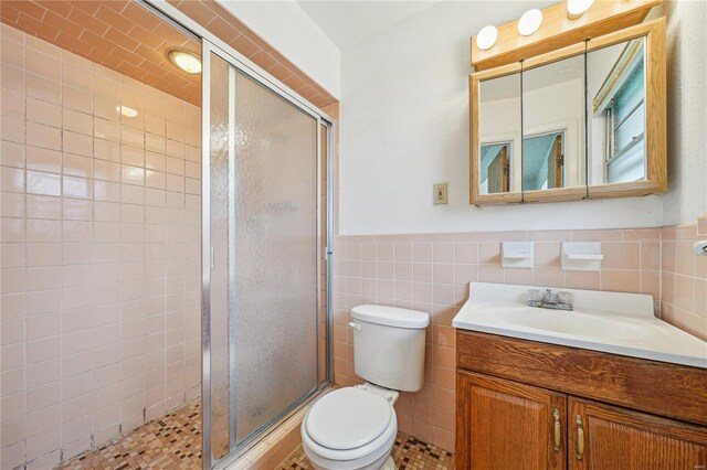 full bath featuring vanity, a stall shower, a wainscoted wall, toilet, and tile walls