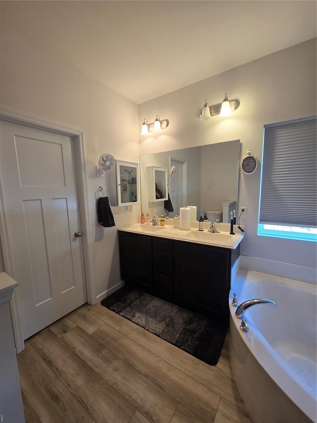 full bathroom with a bath, wood finished floors, double vanity, and a sink