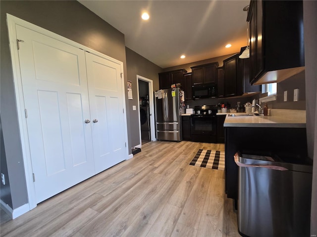 kitchen with light wood-type flooring, recessed lighting, light countertops, black appliances, and a sink