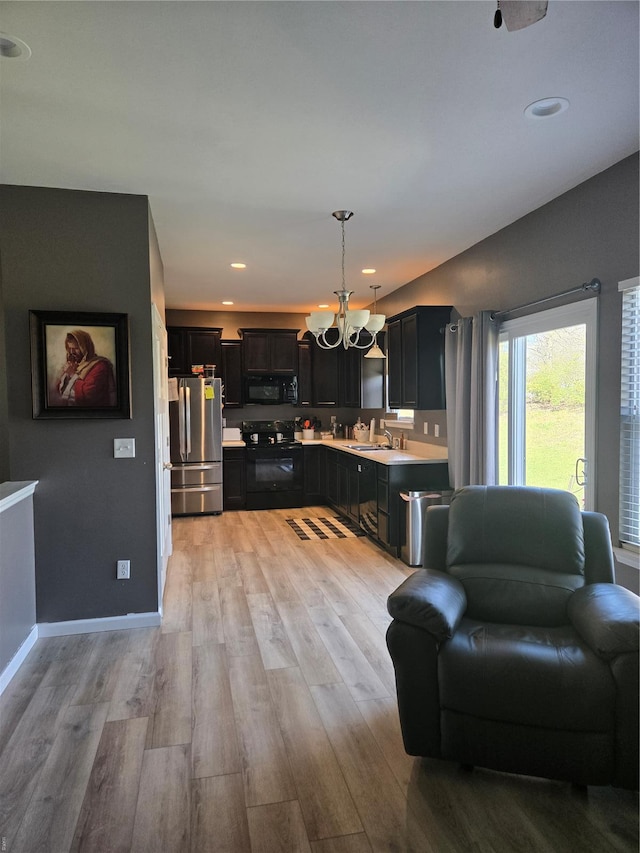 kitchen featuring dark cabinets, a notable chandelier, open floor plan, black appliances, and a sink