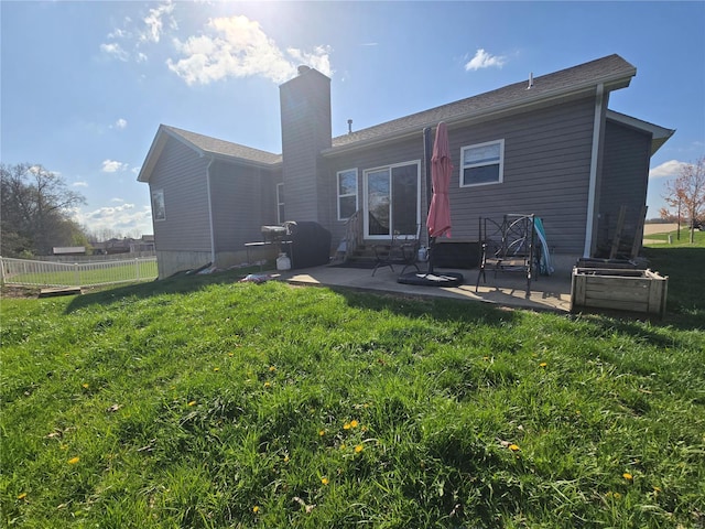 rear view of house featuring fence, a patio, a lawn, and a chimney