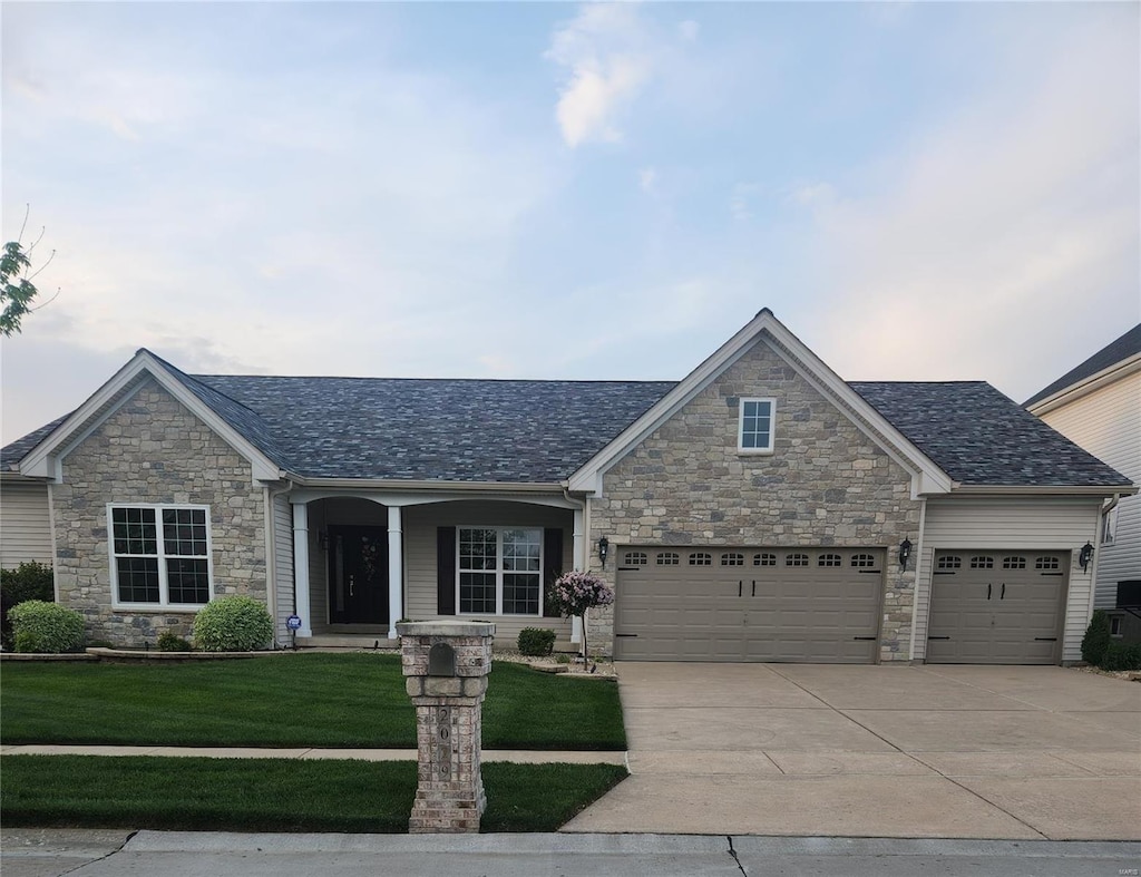 view of front of house featuring a front lawn, a garage, covered porch, driveway, and stone siding
