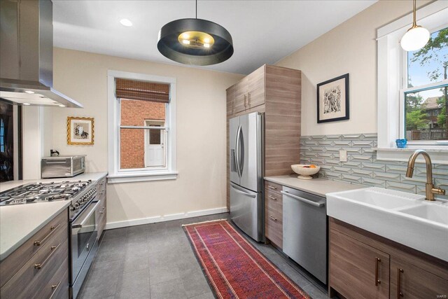 kitchen with decorative backsplash, appliances with stainless steel finishes, a sink, a toaster, and wall chimney exhaust hood