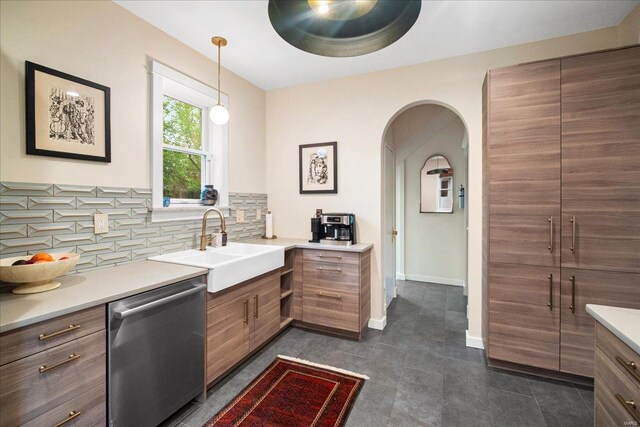 interior space featuring a sink, dishwasher, arched walkways, backsplash, and pendant lighting