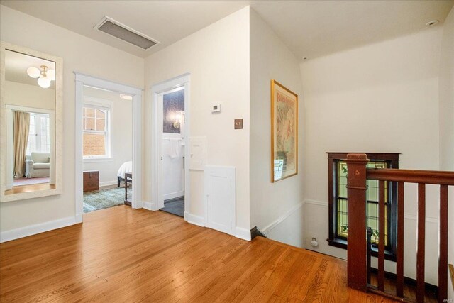 hallway with baseboards, visible vents, wood finished floors, and an upstairs landing