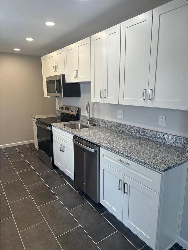 kitchen with dark tile patterned flooring, white cabinets, recessed lighting, a sink, and stainless steel appliances