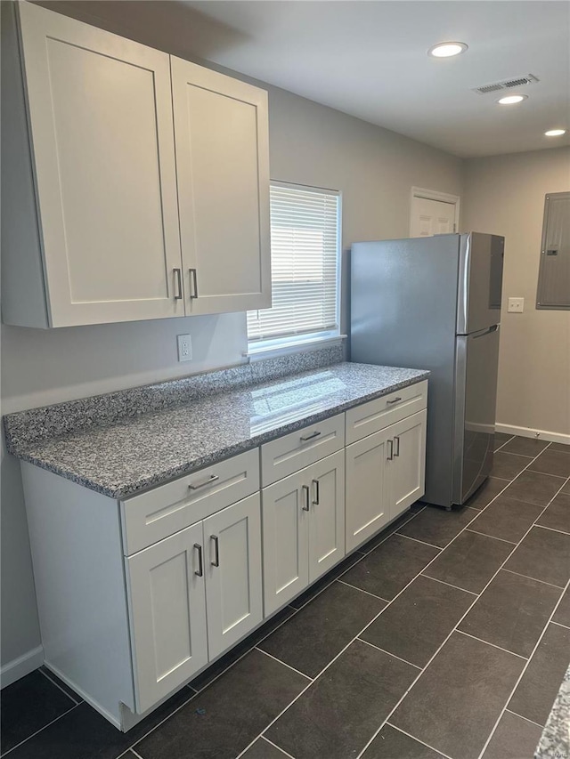 kitchen with electric panel, white cabinetry, freestanding refrigerator, visible vents, and dark tile patterned flooring