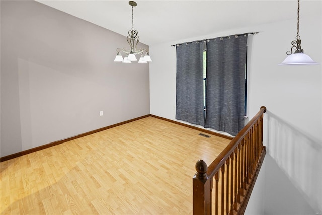 spare room with baseboards, visible vents, wood finished floors, and a chandelier