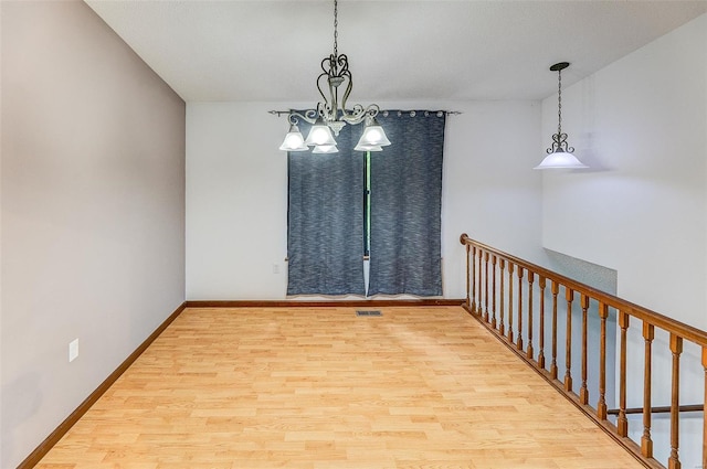 unfurnished room with baseboards, visible vents, wood finished floors, and a notable chandelier