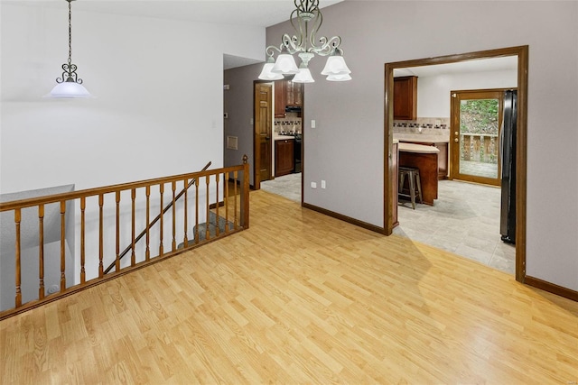 unfurnished room featuring light wood-type flooring, baseboards, a notable chandelier, and vaulted ceiling