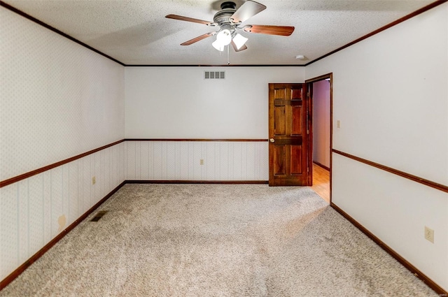 unfurnished room featuring a ceiling fan, a textured ceiling, visible vents, ornamental molding, and light carpet