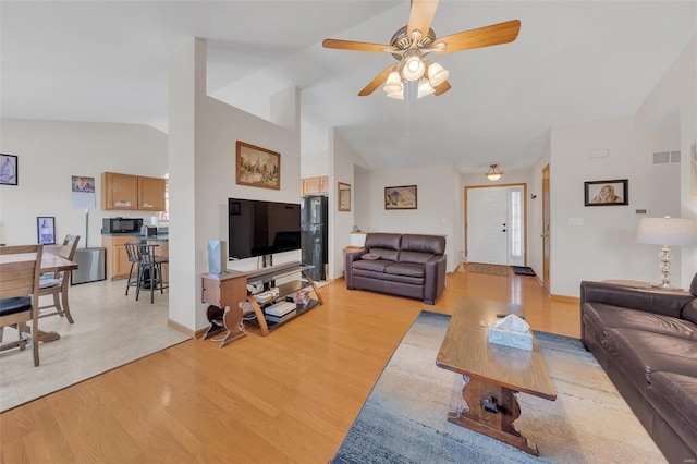 living room with light wood-style floors, visible vents, a ceiling fan, and vaulted ceiling