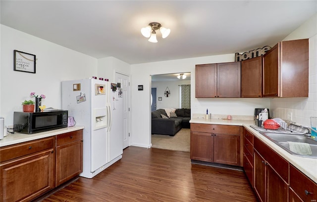 kitchen with dark wood-style flooring, white fridge with ice dispenser, black microwave, light countertops, and a sink