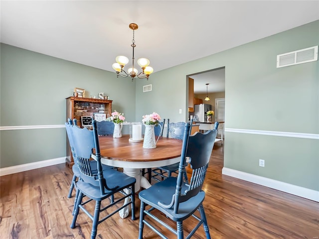 dining area with a chandelier, visible vents, baseboards, and wood finished floors