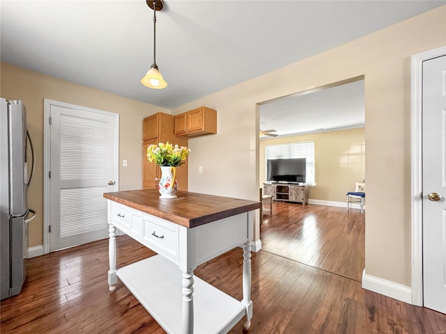 kitchen featuring hanging light fixtures, baseboards, freestanding refrigerator, dark wood finished floors, and wood counters
