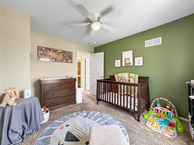 carpeted bedroom with baseboards, a ceiling fan, visible vents, and a crib