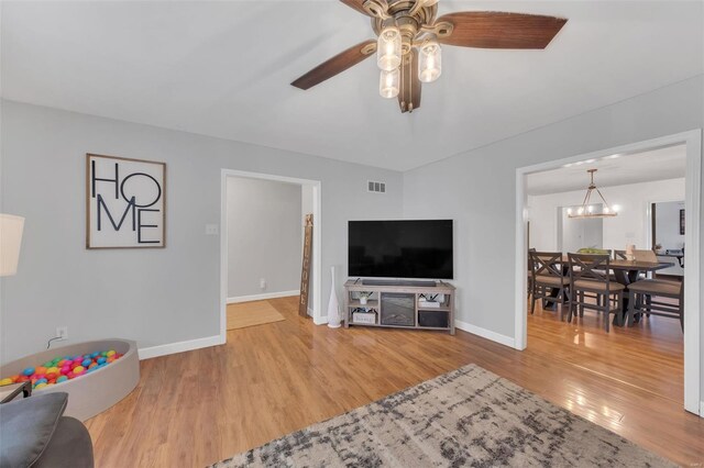 living area with visible vents, baseboards, light wood-style floors, and ceiling fan with notable chandelier