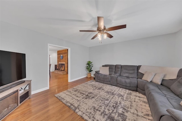 living area with a large fireplace, light wood-style flooring, baseboards, and ceiling fan