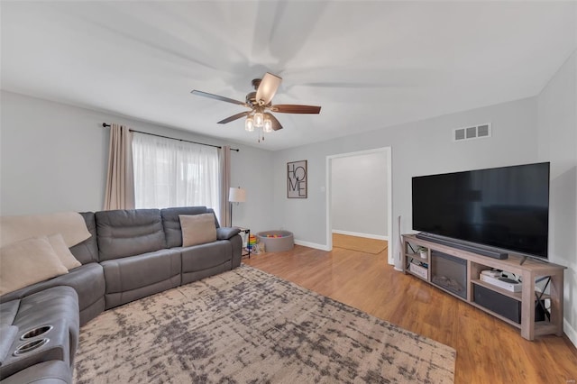 living area with visible vents, baseboards, wood finished floors, and ceiling fan