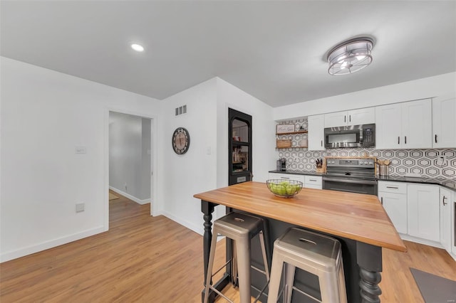 kitchen with white cabinets, stainless steel appliances, a breakfast bar, and butcher block countertops
