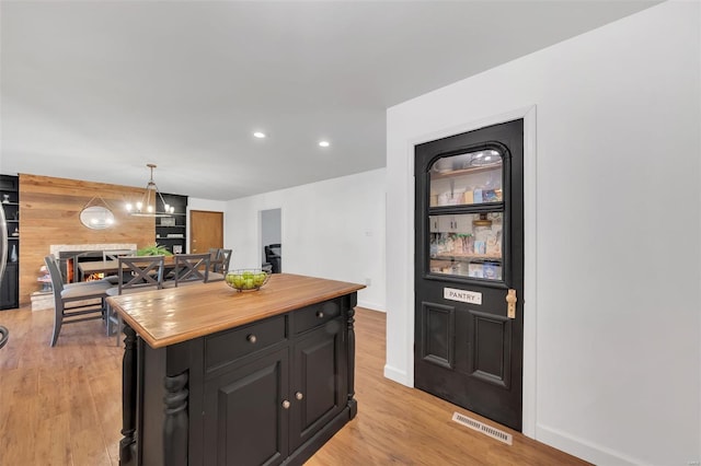 kitchen featuring dark cabinets, butcher block counters, light wood-type flooring, recessed lighting, and a center island