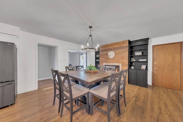 dining space featuring a chandelier, light wood-style floors, a large fireplace, and baseboards