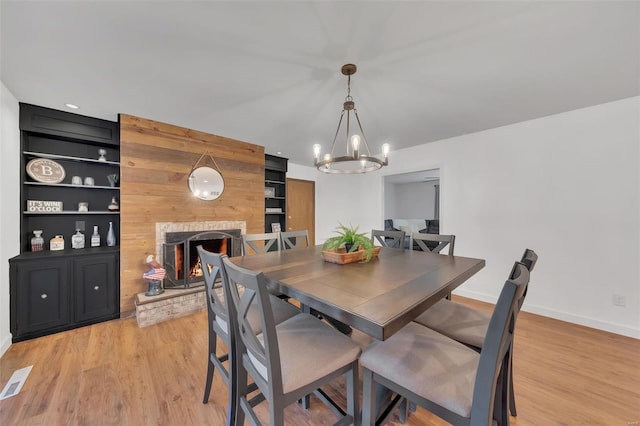 dining room with light wood-style flooring, visible vents, baseboards, a notable chandelier, and a warm lit fireplace