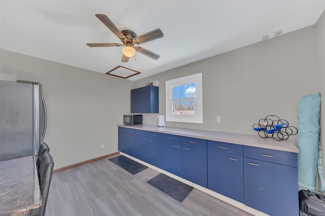 kitchen with baseboards, light wood-type flooring, freestanding refrigerator, a ceiling fan, and blue cabinets