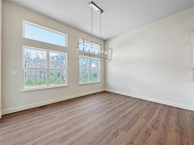unfurnished dining area with baseboards, a notable chandelier, and wood finished floors