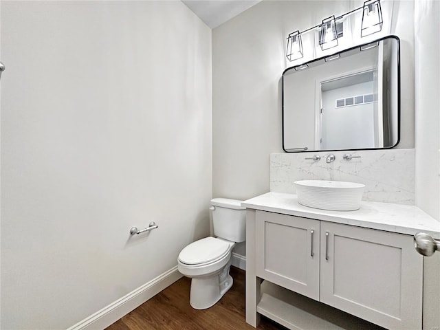 bathroom with tasteful backsplash, vanity, baseboards, toilet, and wood finished floors