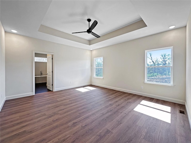unfurnished bedroom featuring visible vents, baseboards, a raised ceiling, dark wood-style floors, and connected bathroom