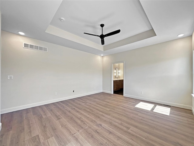 spare room with a tray ceiling, baseboards, a ceiling fan, and visible vents