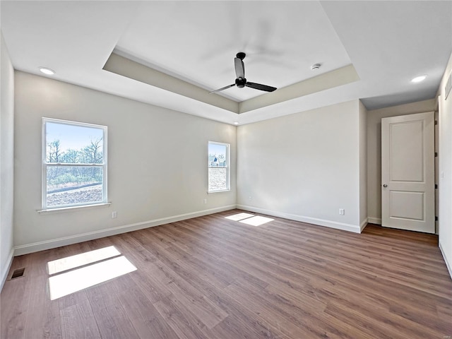 spare room featuring visible vents, baseboards, wood finished floors, and a raised ceiling