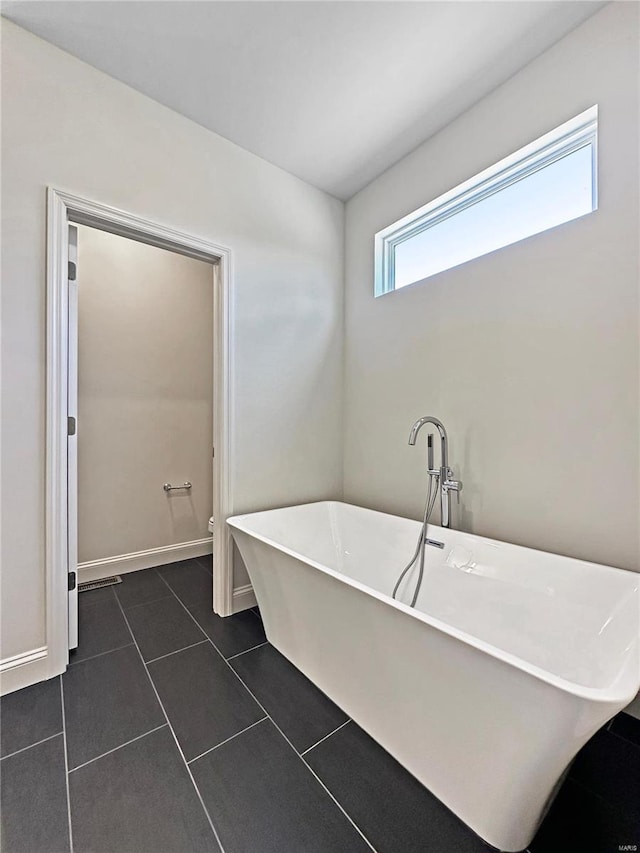 bathroom with a freestanding bath, tile patterned flooring, baseboards, and toilet