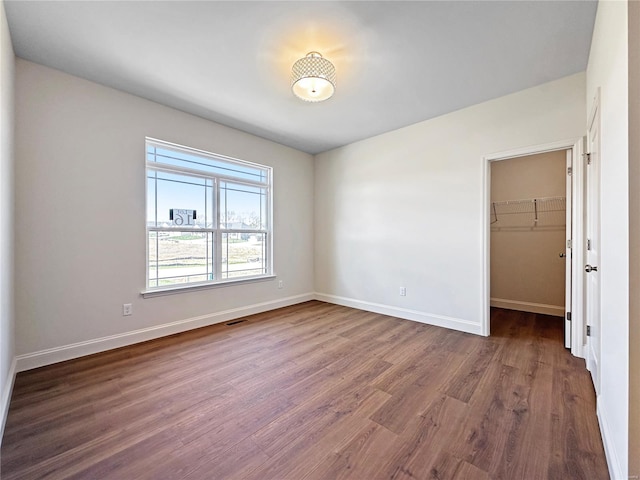 unfurnished bedroom with visible vents, a closet, baseboards, a walk in closet, and wood finished floors