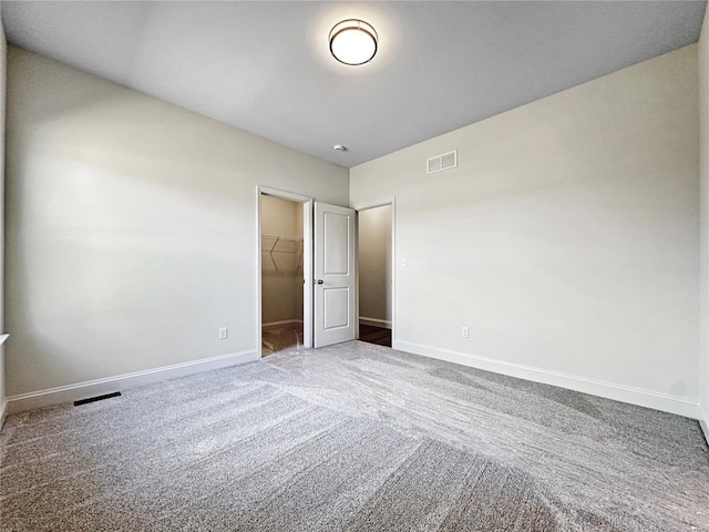 unfurnished bedroom featuring a spacious closet, carpet flooring, visible vents, and baseboards