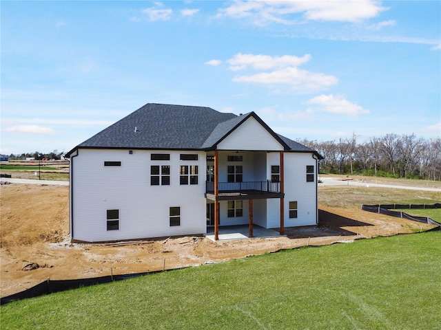 rear view of house with a patio area, a lawn, and roof with shingles