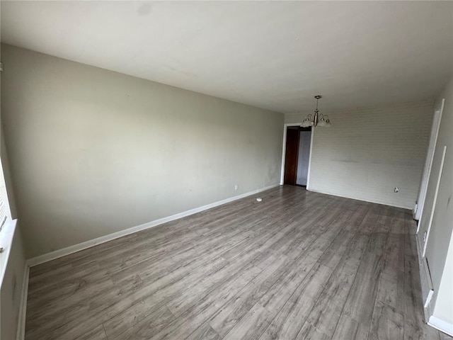 empty room with dark wood-style flooring, baseboards, a notable chandelier, and brick wall