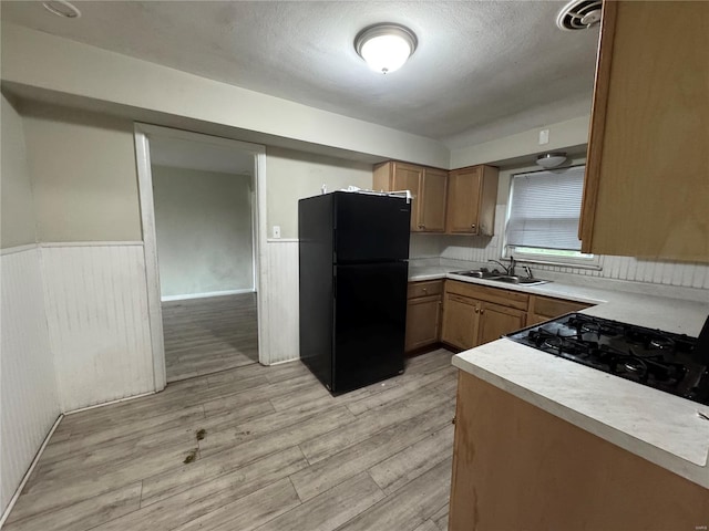 kitchen with light wood-type flooring, light countertops, freestanding refrigerator, a wainscoted wall, and a sink