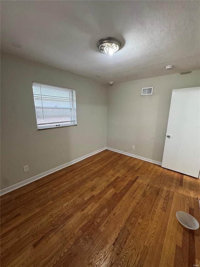 unfurnished room with visible vents, baseboards, a textured ceiling, and wood finished floors