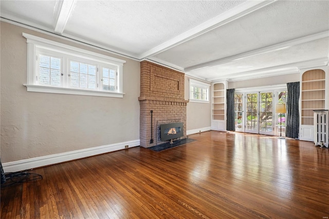 unfurnished living room with a textured ceiling, baseboards, beamed ceiling, a fireplace, and wood-type flooring